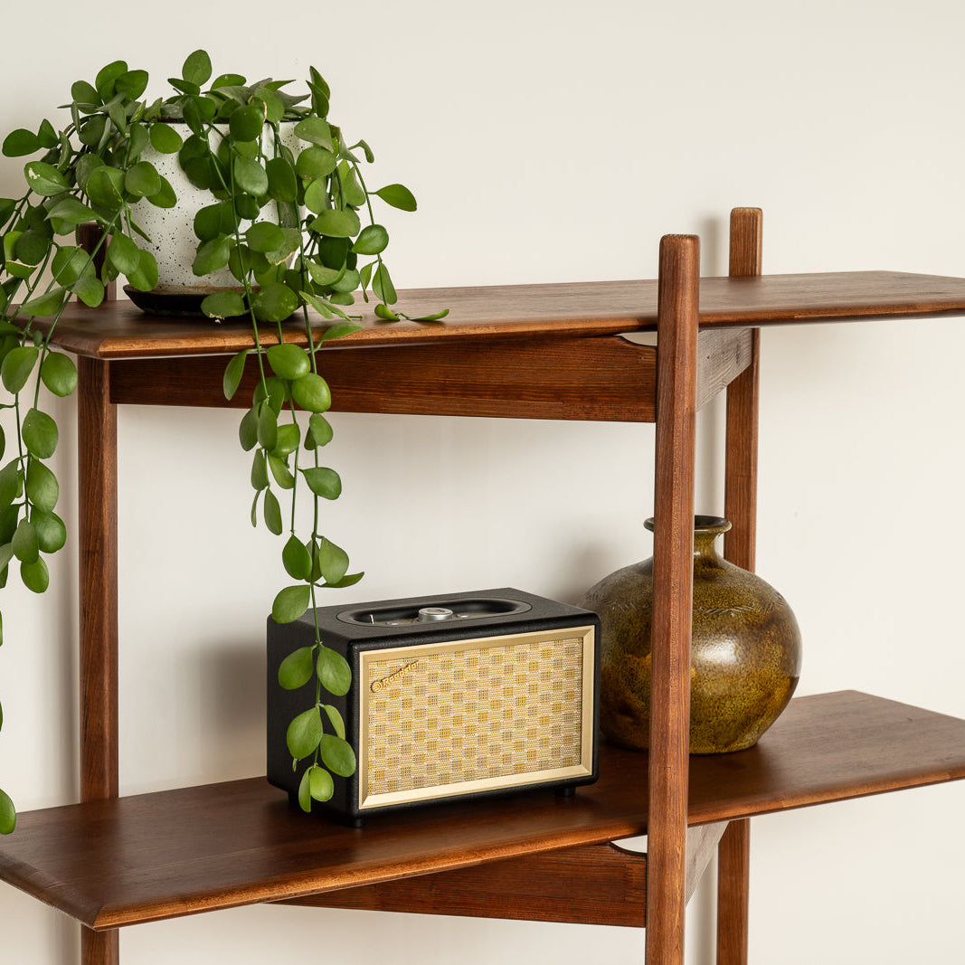Wooden shelf with a plant, radio, and vase against a white wall