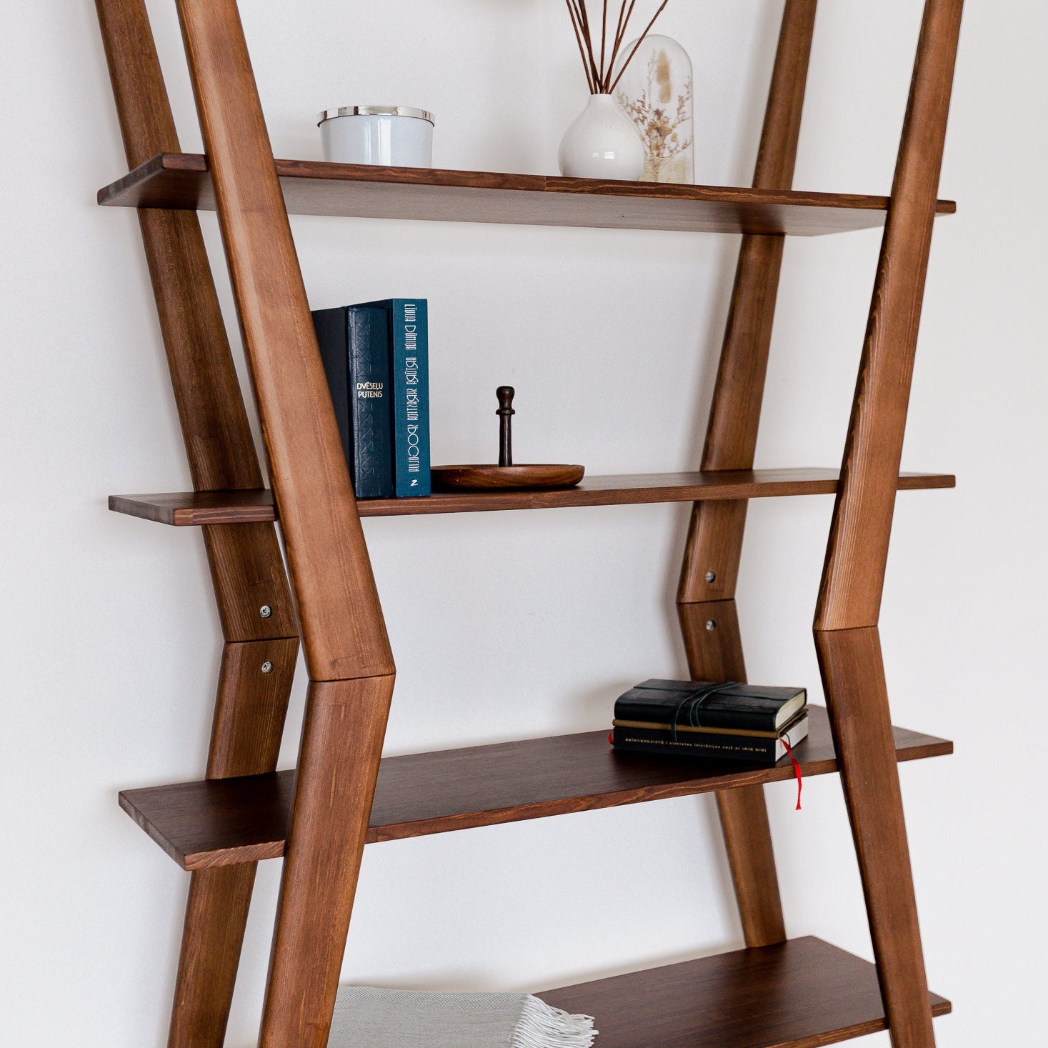 Wooden ladder shelf with books and decorative items against a white wall